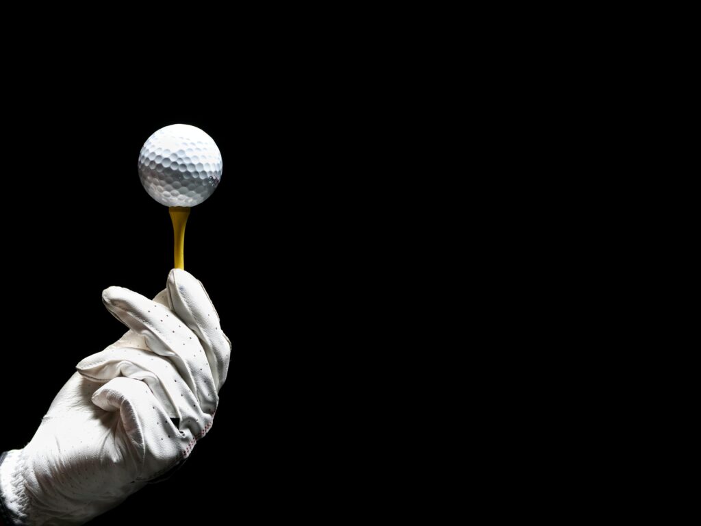Close-up of a golf ball on a tee held by a gloved hand on a black background.